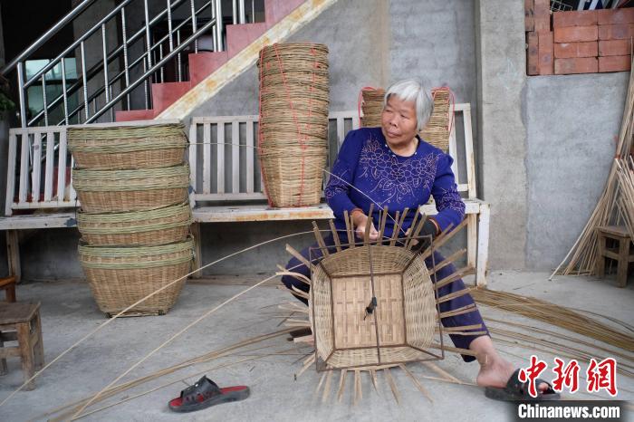 覃氏正在家门屋檐下编织竹筐。 刘俊聪 摄 覃氏正在家门屋檐下编织竹筐。 刘俊聪 摄