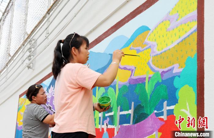 图为侗族农民画家正在外墙上绘制农民画。　龚普康 摄