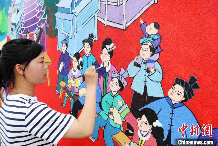图为侗族农民画家正在外墙上绘制农民画。　龚普康 摄